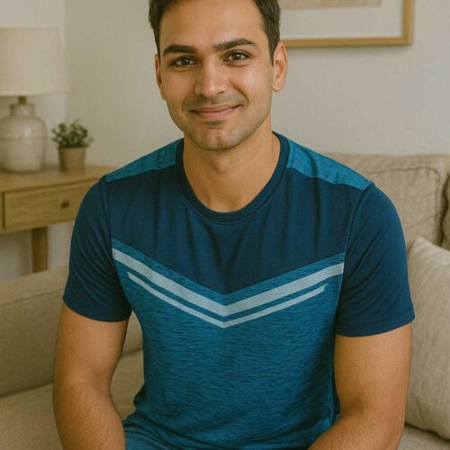 A male client is seated on a beige sofa in a modern living room, wearing a blue t-shirt with chevron stripes and blue jeans. The background features a minimalist decor with a side table, potted plant, ceramic vase, and abstract wall art.