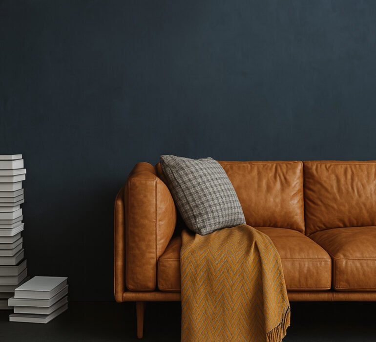 Dark textured wall with a brown leather sofa, stacked books, and a cozy throw blanket in a modern living room.