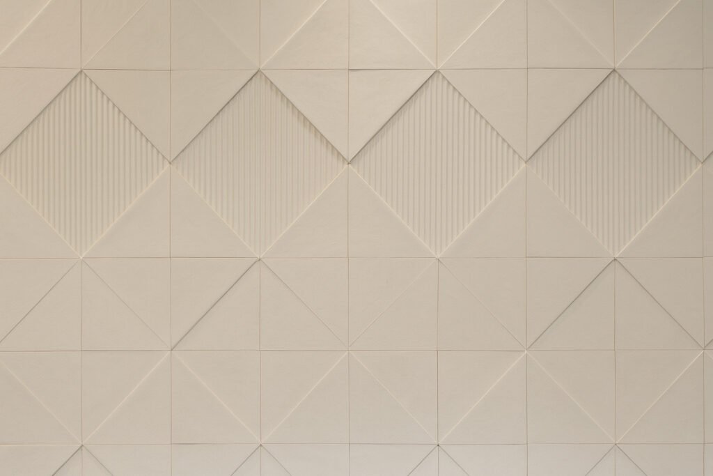 Minimalist 3D geometric wall texture in soft beige, featuring diamond and square patterns with subtle linear and raised details.