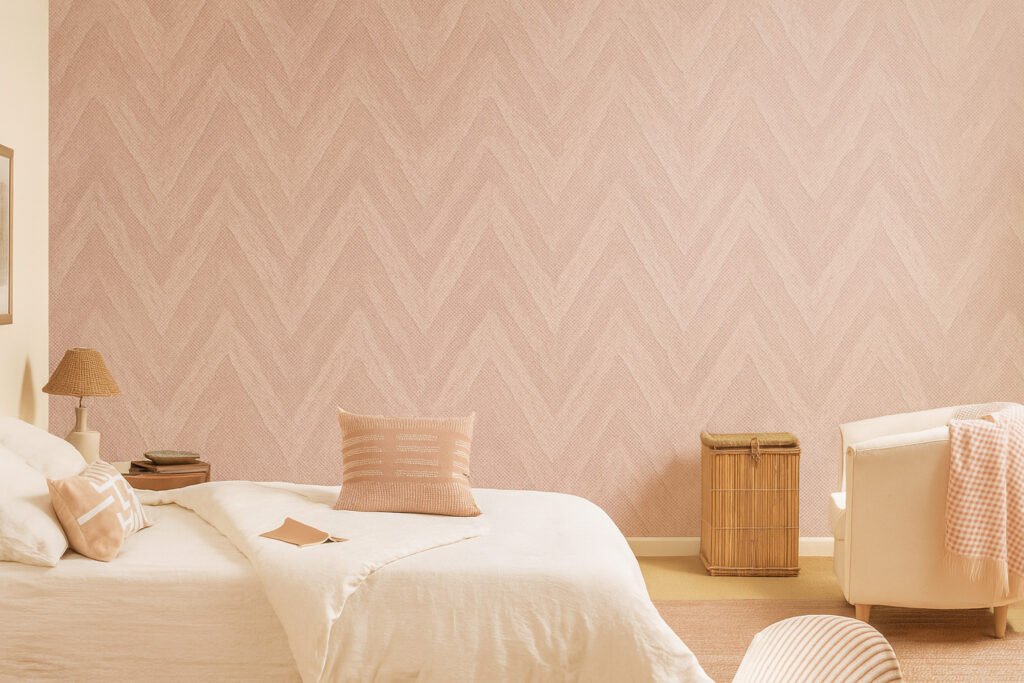Peach-pink textured wall with a subtle chevron pattern, styled in a cozy bedroom setup with neutral bedding and wooden accents.